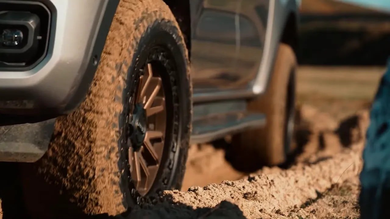 All-terrain tire driving through loose dirt and gravel near the fender