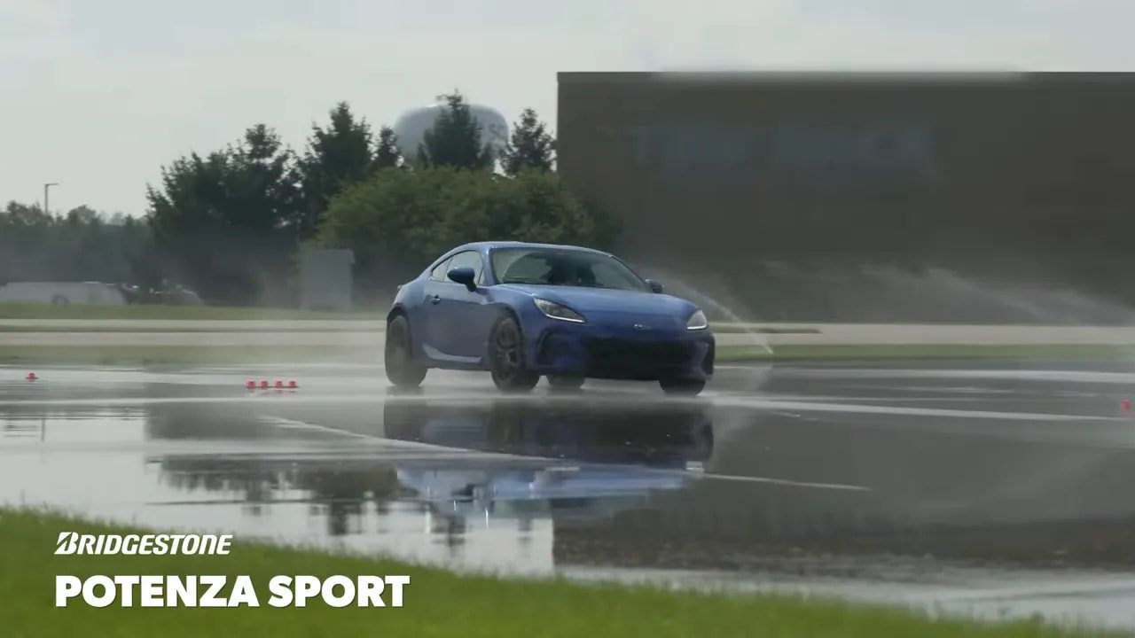 Blue sports car driving through standing water on a track with Bridgestone Potenza Sport branding