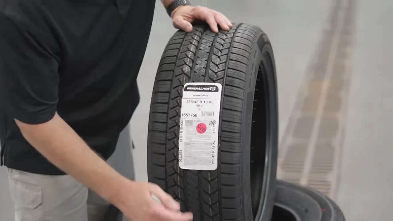 Person holding an all-season tire showing sidewall size and specs