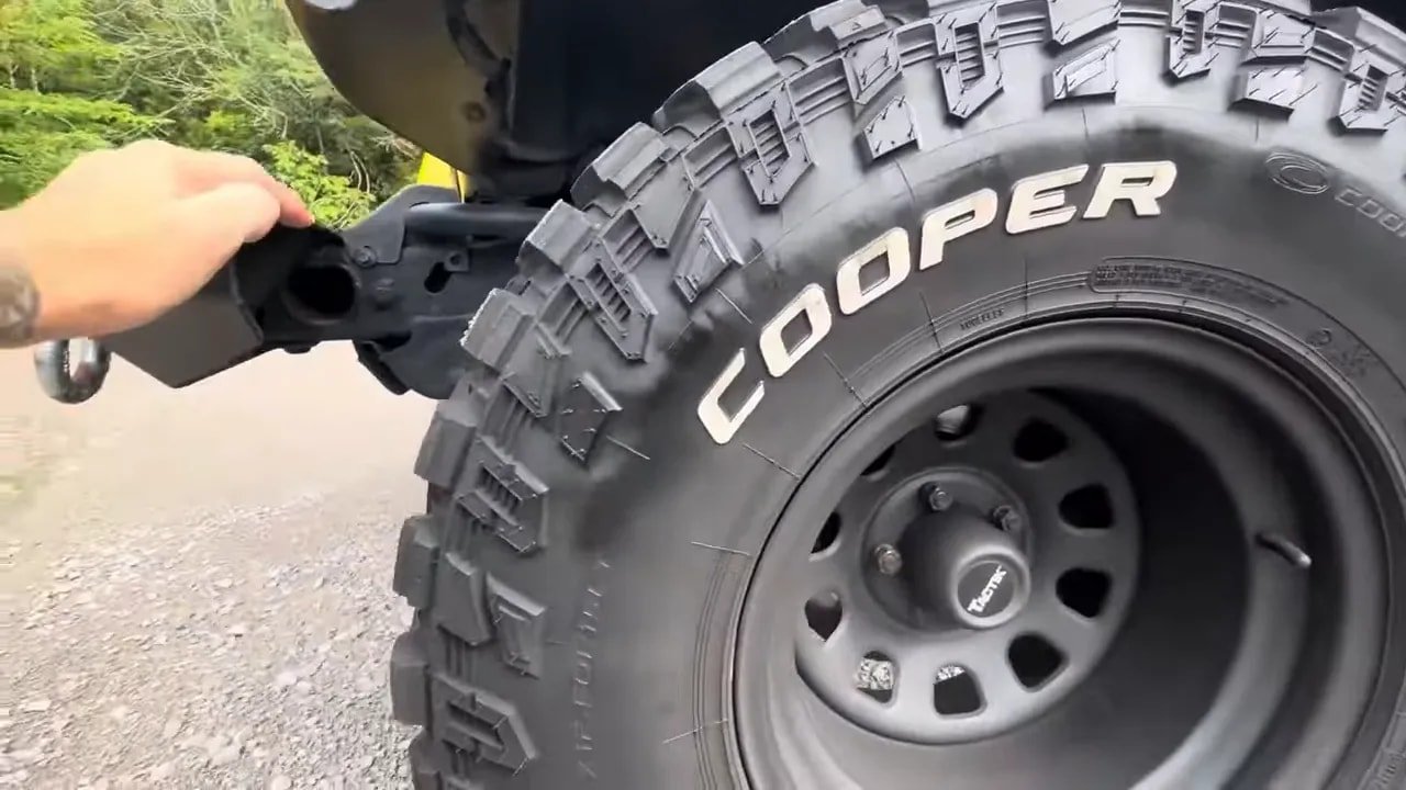 Close-up of mud-terrain tire tread blocks and sidewall lugs with a vehicle in the background