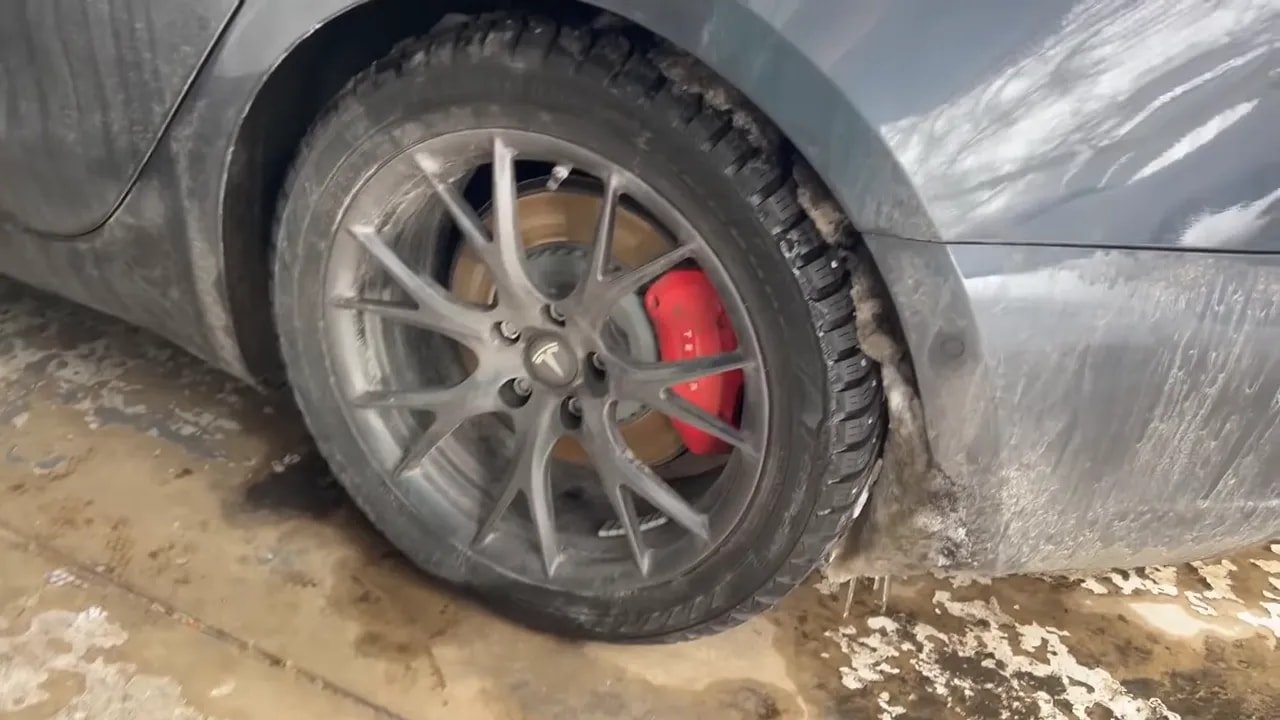 Close-up of a studded winter tire tread and metal studs on a winter road