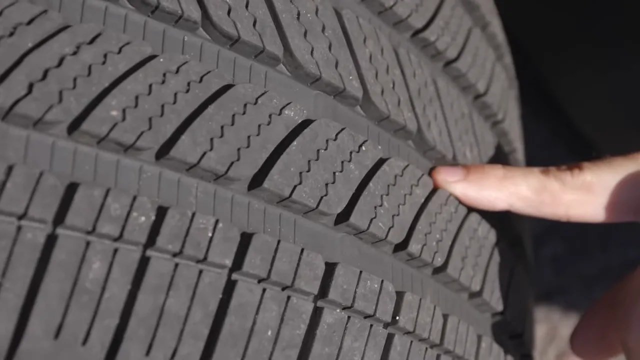 Close-up of car tire tread grooves and sipes being inspected with a hand