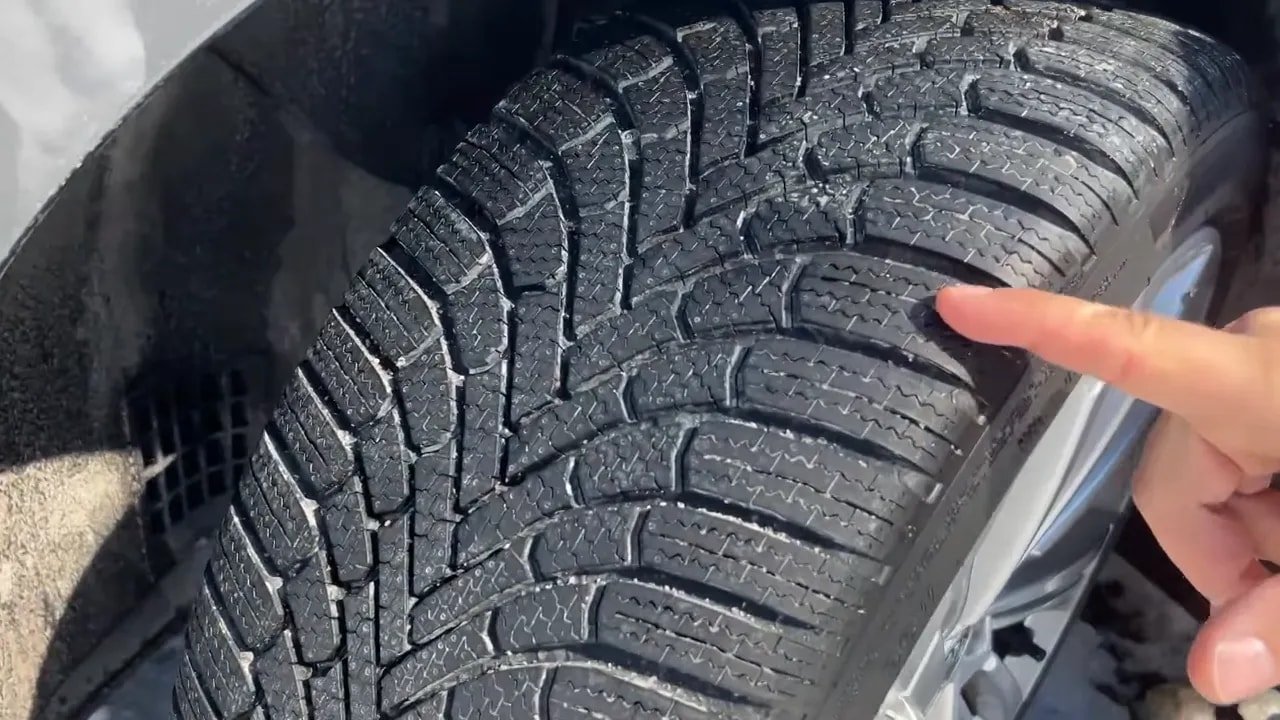 Detailed view of a winter tire tread pattern with finger pointing