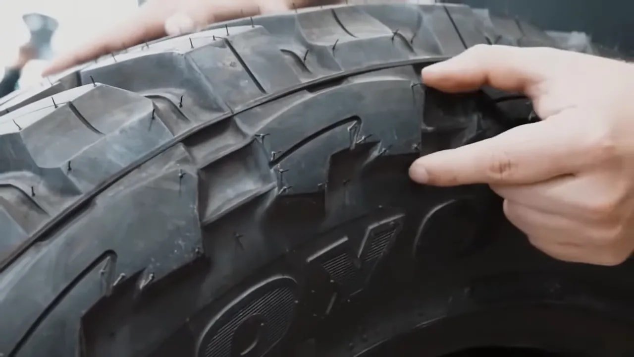 Hand pointing at aggressive mud-terrain tire tread blocks and sidewall lug areas